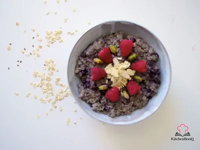 A bowl of creamy blueberry almond porridge topped with fresh blueberries, a swirl of almond butter, and a dusting of cinnamon on a wooden table