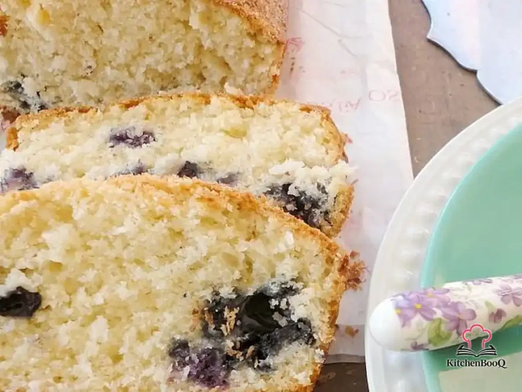 Sliced blueberry and coconut loaf on a wooden board, topped with desiccated coconut and fresh blueberries