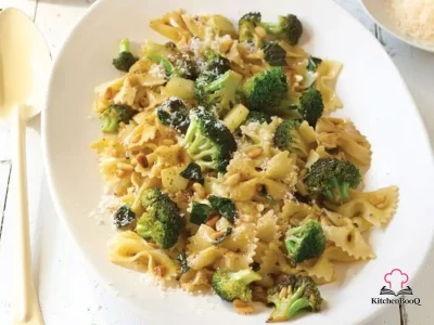 A bowl of bow-tie pasta tossed with brown butter, broccoli florets, toasted pine nuts and fresh basil, topped with shredded parmesan and a drizzle of olive oil