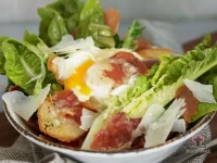 Caesar salad with poached egg, crispy prosciutto, homemade croutons, shaved parmesan and anchovy dressing on a white plate