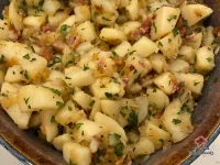 Warm German potato salad with crispy bacon crumbles and fresh parsley in a white serving bowl