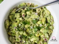 Bowl of avocado tuna salad with chunks of apple, red onion, celery, and toasted walnuts on a white background