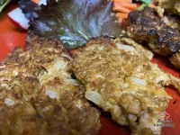 Two golden-brown BBQ tuna fritters served on a white plate garnished with sliced green onions and a side of barbecue dipping sauce