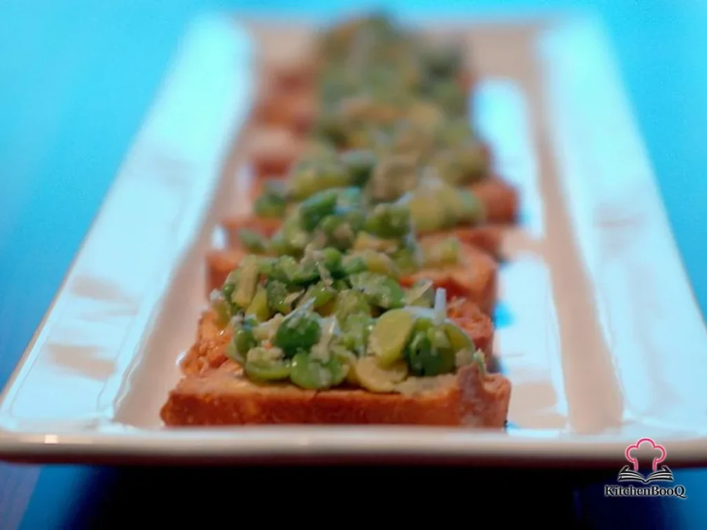 Crispy crostini topped with bright green baby fava beans and shaved parmesan on a wooden serving board