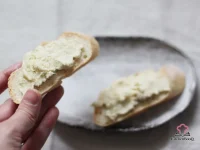 Creamy baccalà mantecato salt cod spread served on slices of grilled polenta, garnished with chopped parsley, on a rustic wooden board