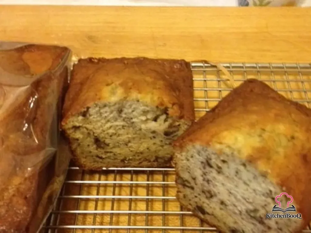 Sliced banana bread with spiced pecans on a wooden cutting board, showing a moist golden crumb studded with chopped pecans