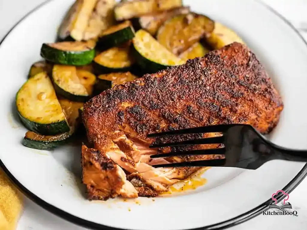 Four pieces of blackened Cajun salmon with a dark spiced crust served alongside tender sautéed zucchini rounds in a cast iron skillet