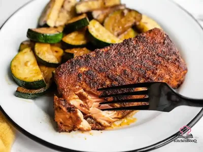 Four pieces of blackened Cajun salmon with a dark spiced crust served alongside tender sautéed zucchini rounds in a cast iron skillet