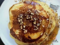 Stack of fluffy egg nog pancakes topped with warm bourbon-maple syrup and a dusting of freshly ground nutmeg on a rustic holiday breakfast table