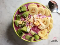A tall glass bowl filled with a creamy green-purple smoothie blend made from bananas and mixed lettuce, garnished with fresh lettuce leaves