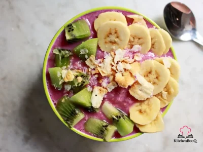 A tall glass bowl filled with a creamy green-purple smoothie blend made from bananas and mixed lettuce, garnished with fresh lettuce leaves