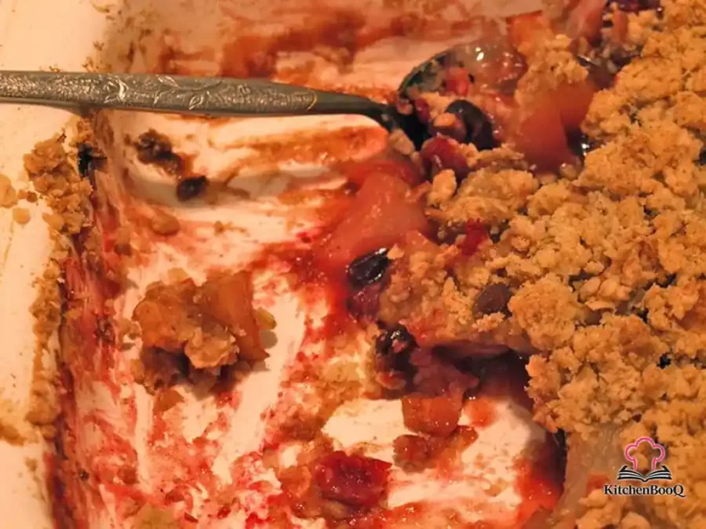 Golden oat-pecan crisp topping over bubbling apples, pears, and cranberries in a rustic baking dish served with cream