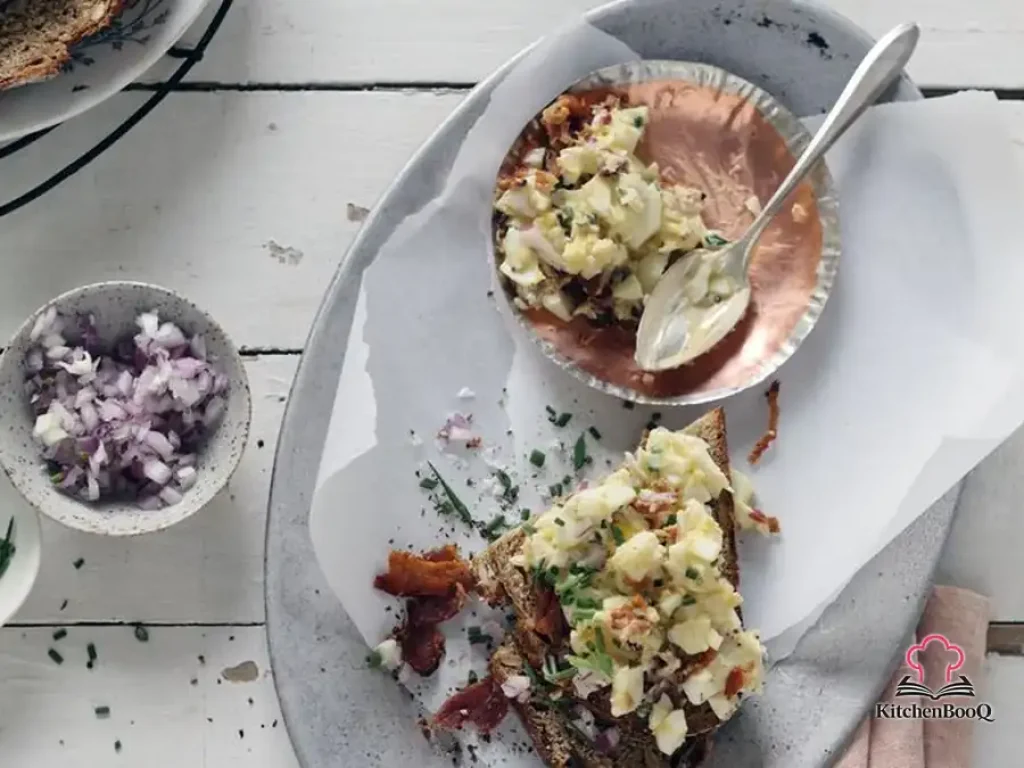 Creamy breakfast egg salad with crumbled bacon and fresh chives served on toasted whole-grain bread on a white plate