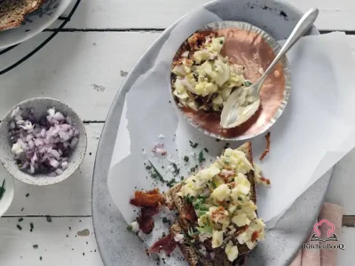 Creamy breakfast egg salad with crumbled bacon and fresh chives served on toasted whole-grain bread on a white plate