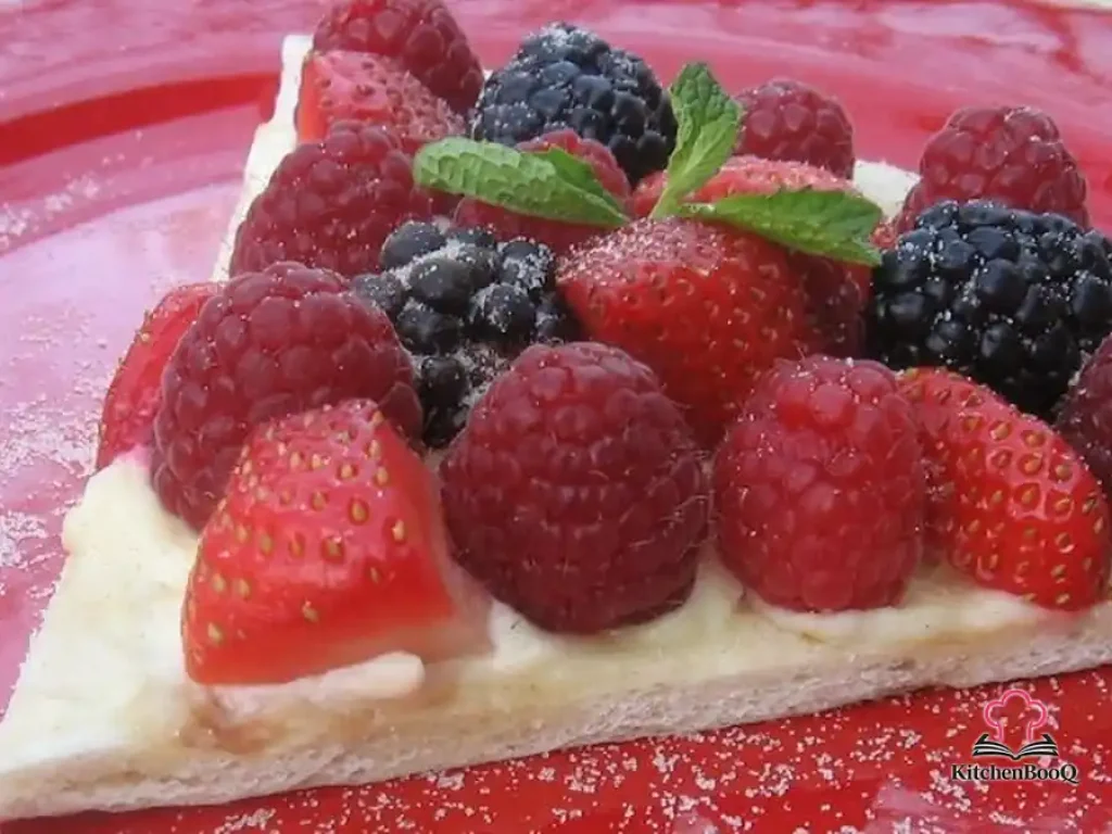 Overhead view of a breakfast pizza topped with creamy lemon mascarpone, fresh mixed berries including strawberries, blueberries and raspberries, and tiny mint sprigs on a golden cinnamon-sugar crust