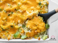 A golden-topped broccoli cheddar rice casserole in a white baking dish with melted cheese bubbling around the edges and bright green broccoli visible beneath