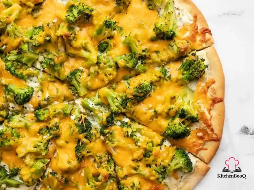 Broccoli cheddar pizza with herby white sauce cut into eight slices on a round pizza pan with melted golden cheddar and bright green broccoli florets