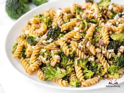 A large bowl of broccoli rotini pasta salad with crumbled feta, red onion, and sunflower seeds drizzled with tomato basil vinaigrette