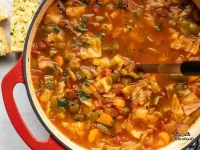 A rustic bowl of hearty cabbage soup filled with colorful vegetables in a rich tomato broth, garnished with fresh parsley and served with crusty bread