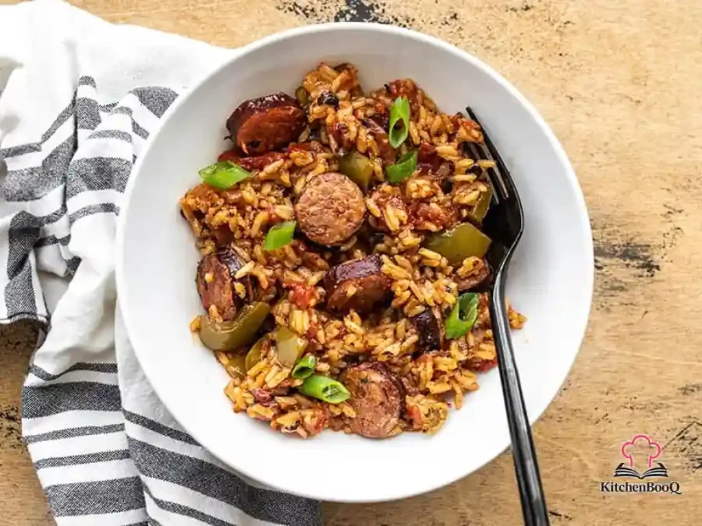 A cast iron skillet filled with Cajun sausage and rice, garnished with sliced green onions, showing golden browned Andouille sausage slices nestled in seasoned red rice