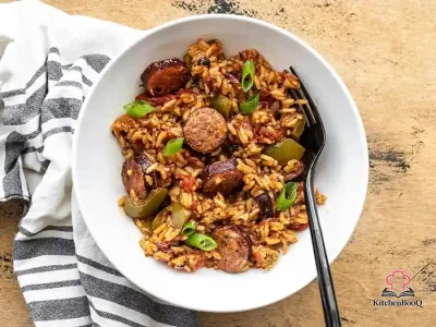 A cast iron skillet filled with Cajun sausage and rice, garnished with sliced green onions, showing golden browned Andouille sausage slices nestled in seasoned red rice