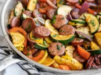 Cajun sausage and vegetable skillet with sliced Andouille sausage, zucchini, yellow squash, red bell pepper, and red onion garnished with fresh parsley