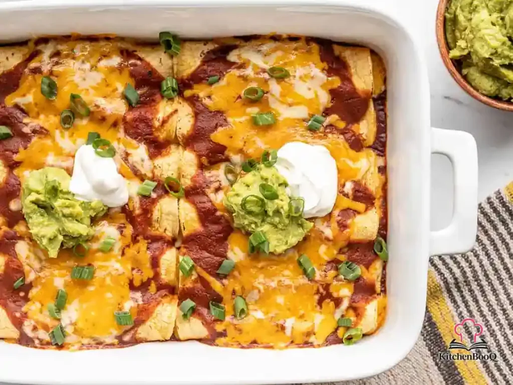 Four cheese enchiladas in a casserole dish smothered in red enchilada sauce and melted shredded cheese, garnished with sour cream and fresh cilantro