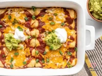 Four cheese enchiladas in a casserole dish smothered in red enchilada sauce and melted shredded cheese, garnished with sour cream and fresh cilantro