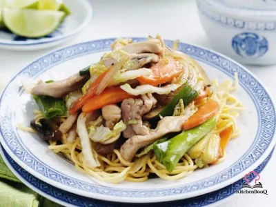 A white bowl of chicken chow mein with fresh noodles, sliced chicken thigh, baby corn, mushrooms, carrots, and green onions in a glossy soy-oyster sauce