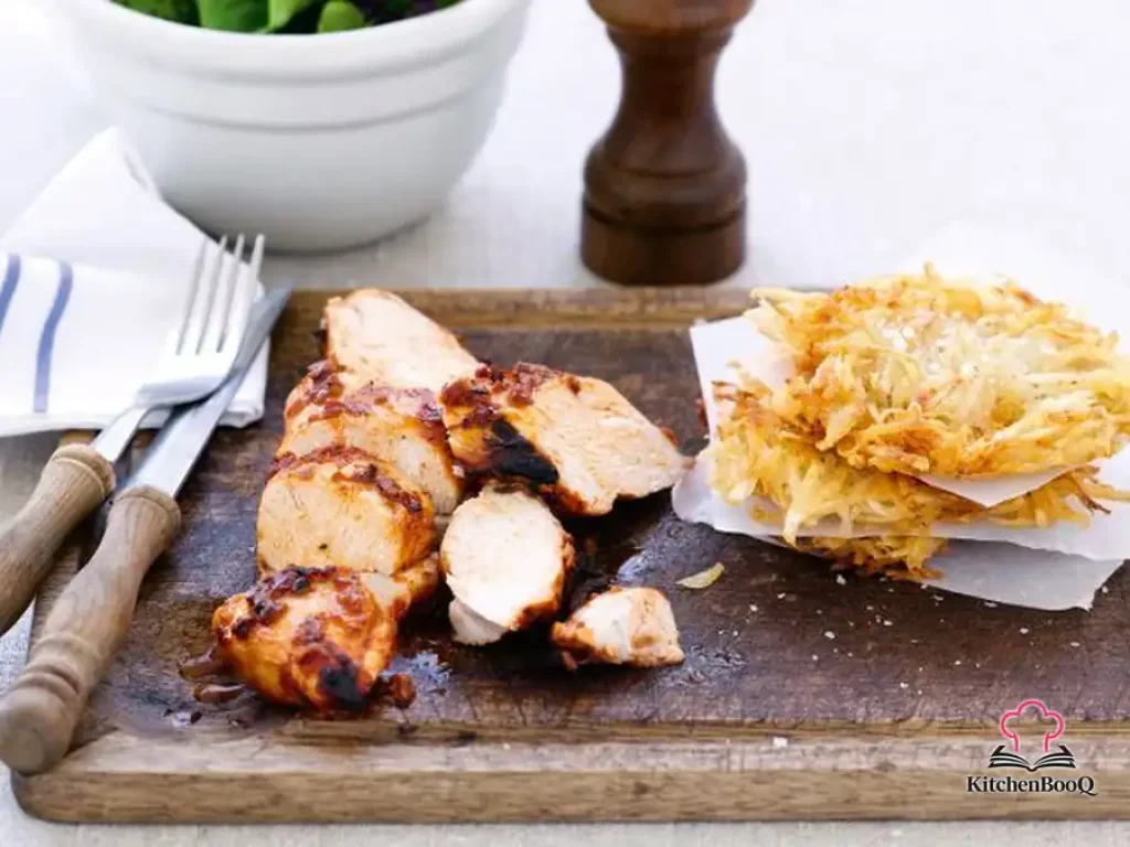 Sliced grilled tapenade chicken served alongside golden crispy potato cakes and fresh mixed salad leaves on a white plate