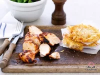 Sliced grilled tapenade chicken served alongside golden crispy potato cakes and fresh mixed salad leaves on a white plate