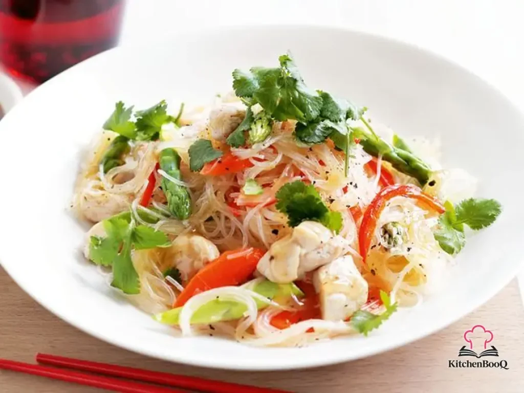 Chicken and vermicelli noodle stir-fry with capsicum, asparagus and carrots garnished with fresh coriander leaves in a white bowl