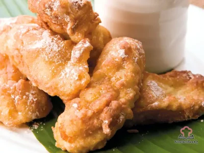 Golden banana fritters stacked on a white plate dusted with powdered sugar and served warm