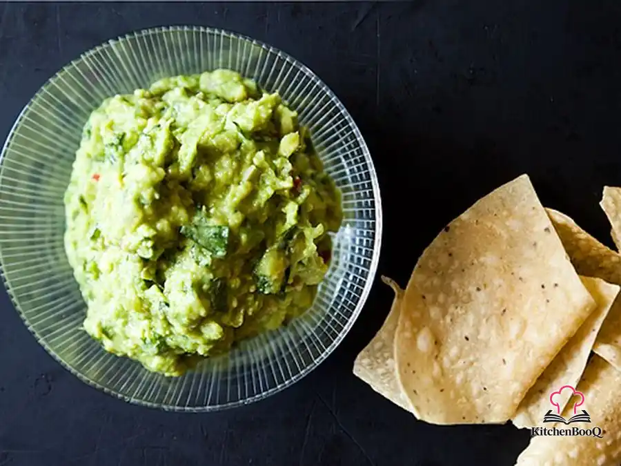 Bowl of Bangkokamole Thai-inspired guacamole topped with fresh mint, Thai basil, cilantro, and sliced red Thai chiles on a wooden board