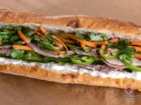 Toasted French baguette banh mi sandwich filled with broiled chicken, pickled carrots and daikon, cucumber slices, fresh cilantro, and jalapeño on a wooden board
