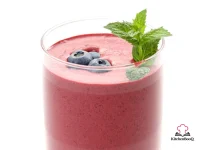 A chilled bowl of vibrant purple berry buttermilk soup garnished with a slice of orange and fresh blueberries