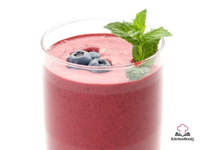 A chilled bowl of vibrant purple berry buttermilk soup garnished with a slice of orange and fresh blueberries