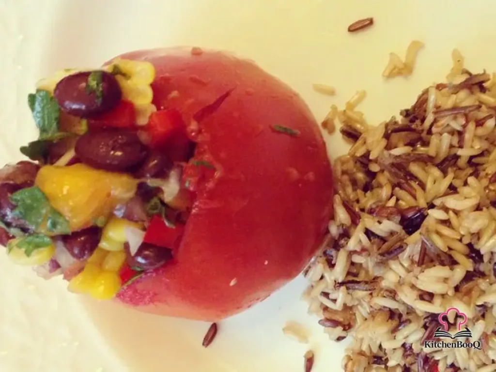 Six large tomatoes stuffed with colorful black bean and mango salsa topped with fresh parsley on a white serving platter