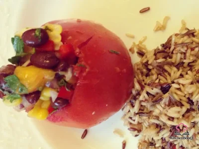Six large tomatoes stuffed with colorful black bean and mango salsa topped with fresh parsley on a white serving platter