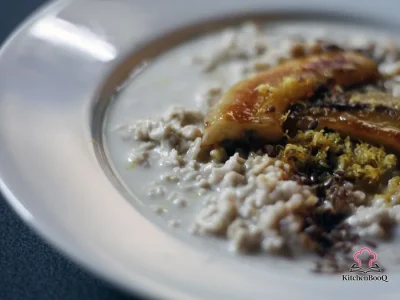 A bowl of creamy coconut milk oatmeal topped with caramelized banana halves, flax seeds, lemon zest, and a drizzle of maple syrup on a rustic wooden surface