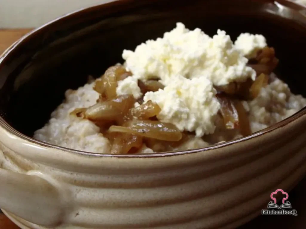 A white bowl of creamy steel cut oats topped with golden caramelized onions and a dollop of fresh white ricotta cheese on a rustic wooden surface