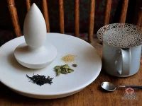 A steaming cup of cardamom chai with frothy milk and whole cardamom pods on a rustic wooden table