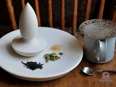 A steaming cup of cardamom chai with frothy milk and whole cardamom pods on a rustic wooden table