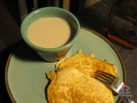 Stack of fluffy carrot cake pancakes topped with whipped cream cheese and drizzled with maple syrup on a rustic wooden plate