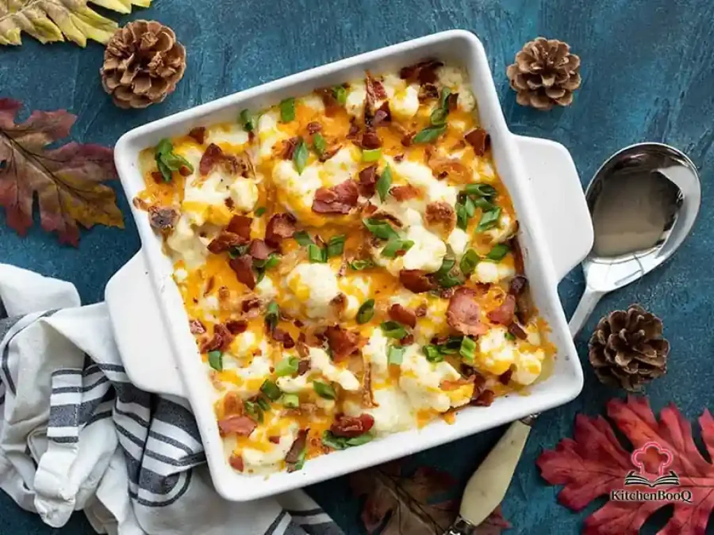 Golden cheesy loaded cauliflower casserole in a white baking dish topped with crispy bacon bits, French fried onions, melted cheddar, and sliced green onions
