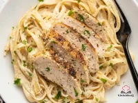 A bowl of creamy chicken Alfredo fettuccine topped with sliced pan-seared chicken breast and garnished with fresh chopped parsley and grated Parmesan