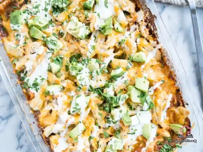 Overhead view of a 9x13 baking dish filled with chicken enchilada casserole topped with melted shredded cheese and crushed tortilla chips with red enchilada sauce visible at the edges