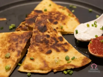 Golden crispy breakfast quesadilla cut in half and filled with a fried egg, melted cheddar cheese, chili garlic sauce, and fresh spinach on a white plate