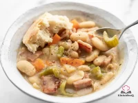 A rustic bowl of chunky ham and bean soup filled with diced ham, white cannellini beans, sliced carrots, and celery in a thick creamy broth, garnished with freshly cracked black pepper