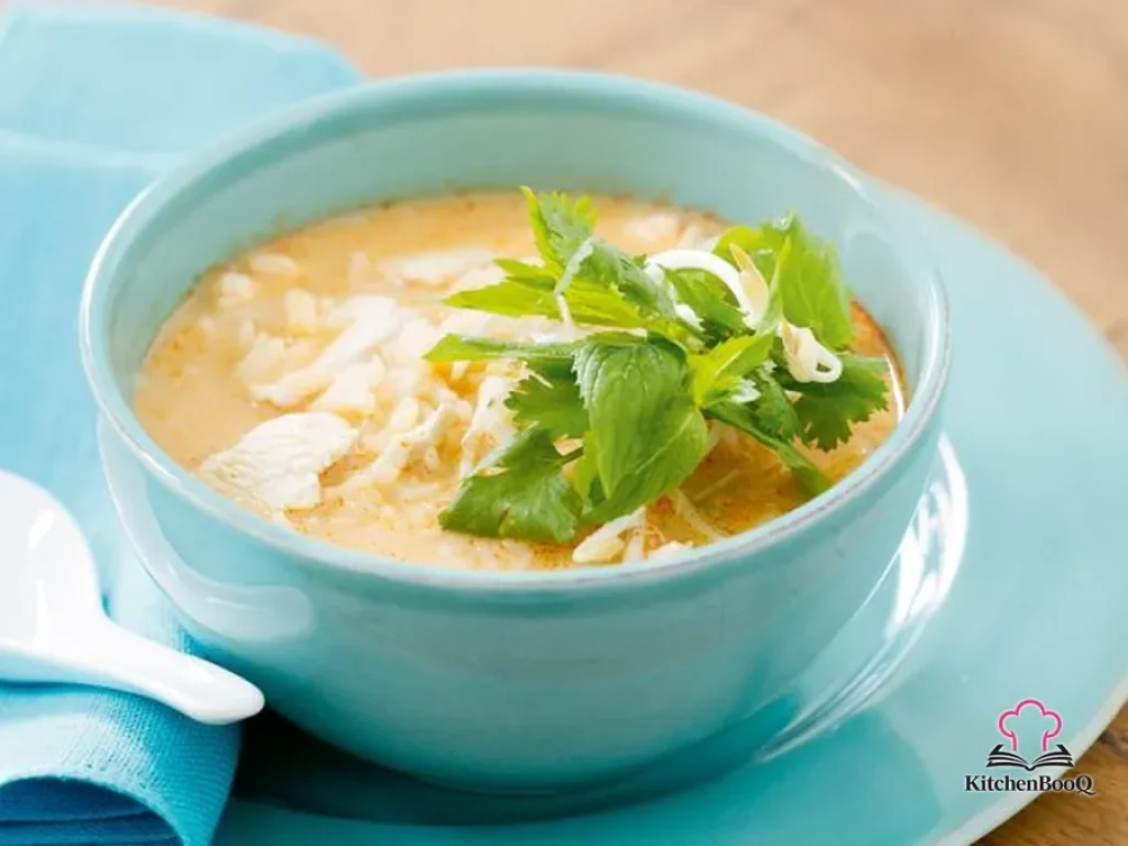 A bowl of coconut chicken and rice soup topped with fresh bean sprouts, mint leaves, and coriander, served in a white bowl with a golden coconut broth